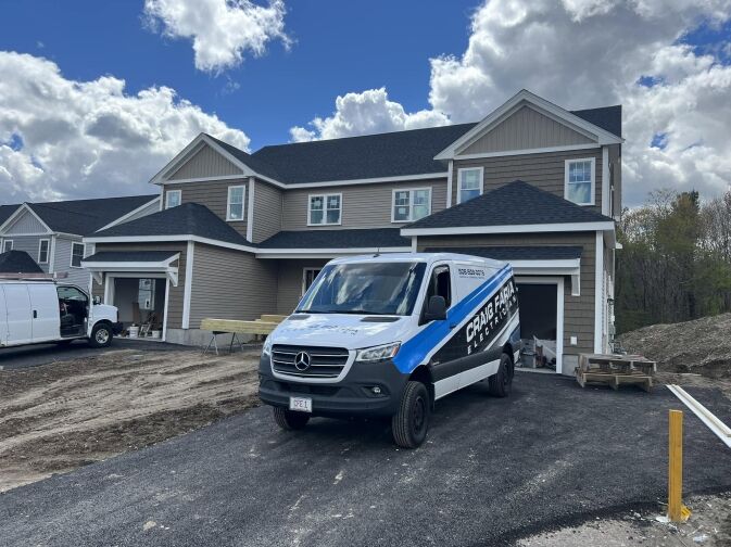 A blue and white van is parked on a newly paved driveway in front of a two-story tan house under construction.