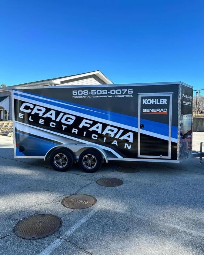 A blue and black trailer labeled “Craig Faria Electrician” with contact information and brand logos is parked on a paved surface near a building.